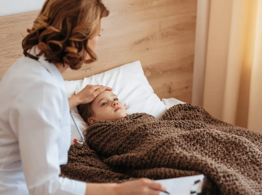 Γιατρός εξετάζει άρρωστο παιδί στο κρεβάτι, ελέγχοντας το μέτωπο για πυρετό σε κατ'οίκον επίσκεψη.