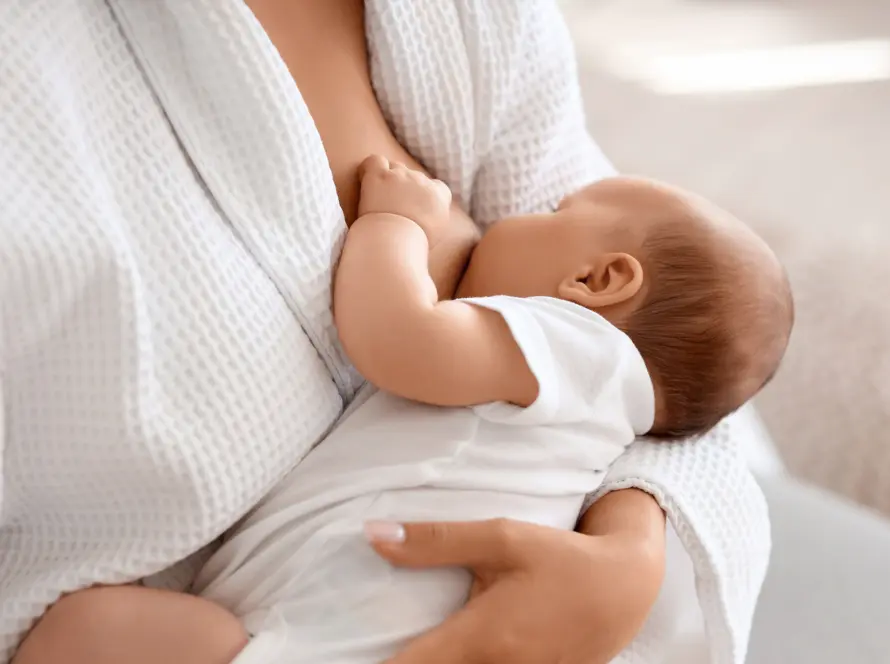 Μητέρα θηλάζει το μωρό της φορώντας λευκή ρόμπα, προβάλλοντας τη στοργή και τη σημασία του μητρικού θηλασμού.