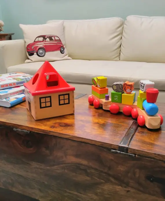 Η παιδίατρος 9 Ξύλινο τραπέζι με παιδικά εκπαιδευτικά παιχνίδια, βιβλία, ξύλινο σπιτάκι και πολύχρωμη ξύλινη αμαξοστοιχία, σε άνετο παιδικό χώρο αναμονής.